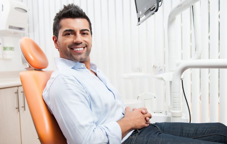 A man with beautiful smile sitting in a dental chair after restorative cosmetic dental treatment