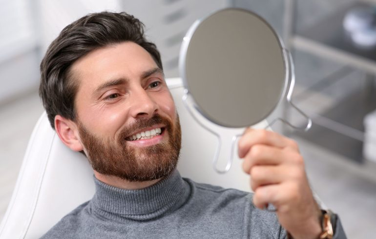 A satisfied man in a dental chair looking at his new dental implants in a mirror