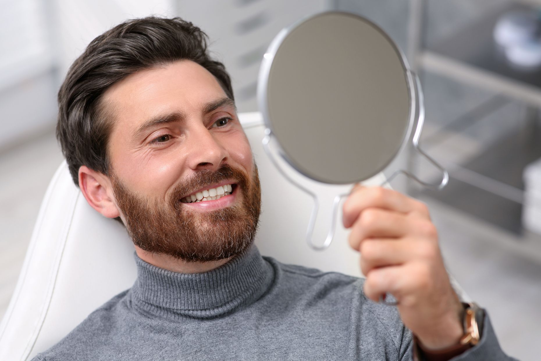 A satisfied man in a dental chair looking at his new dental implants in a mirror